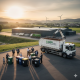 Ein LKW der AER GmbH mit Container und verschiedene Mülltonnen zur Abfalltrennung vor einem modernen Recyclinghof in Hessen bei Sonnenuntergang.